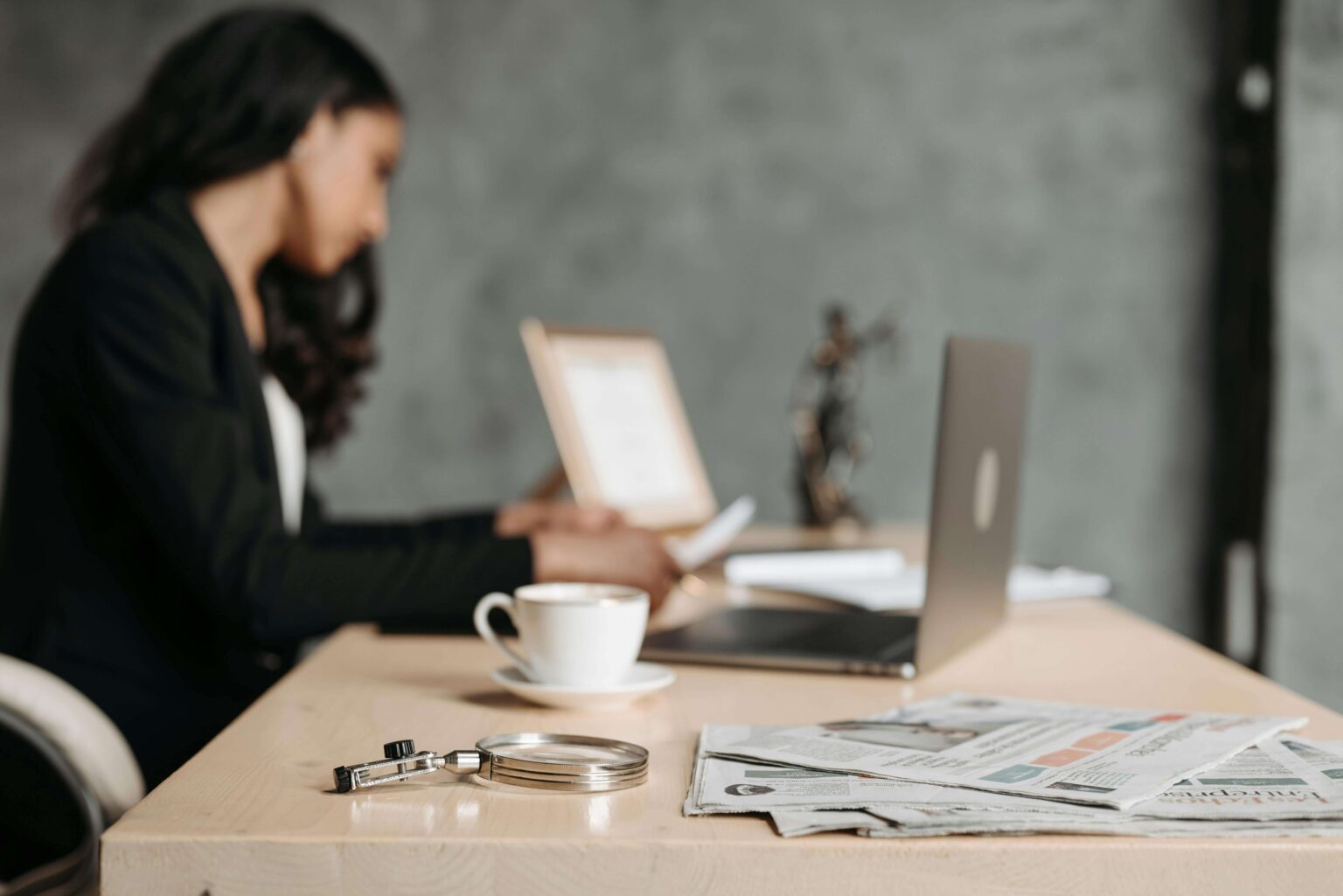 Woman working at a desk with magnifying glass and papers resting on it